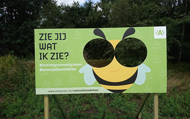 Reclamebord waar een bij op staat. De oogjes zijn uitgesneden zodat je erdoor kan kijken.